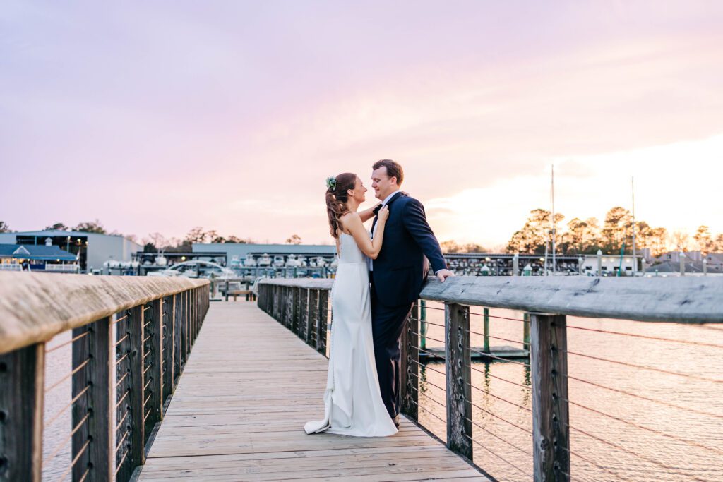 Couple leans in for a kiss at the docks at Airlie Gardens